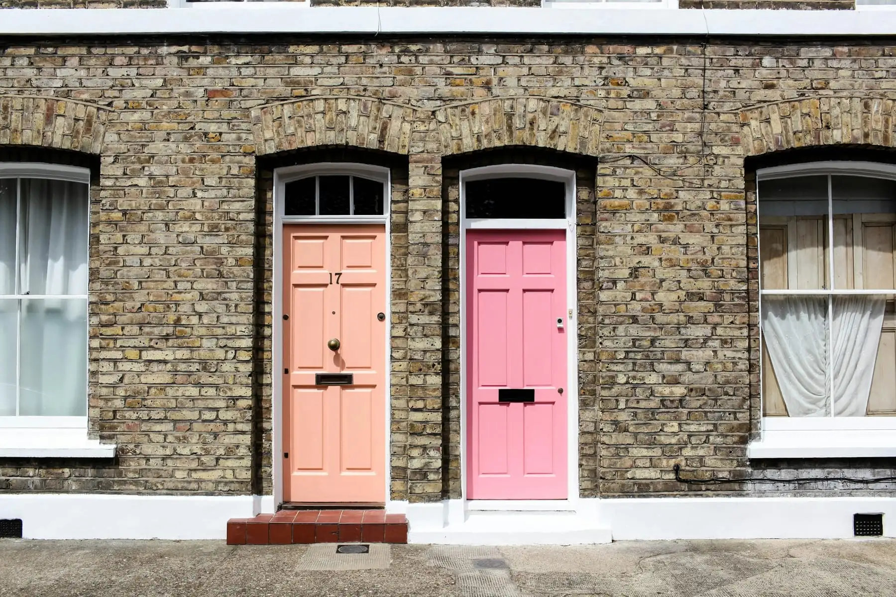 Two neighbouring front doors, one peach and one pink, in a London brick terrace